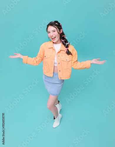 Asian woman with open arms posing in studio expressing confidence positivity and carefree youthful lifestyle energy for modern fashion and empowerment isolated on blue background.