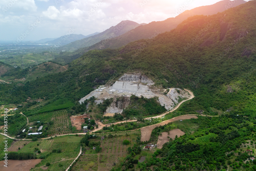 Fototapeta premium Aerial view shows a quarry on a hillside in Southeast Asia where large blocks of stone are being extracted and moved by machinery. Heavy equipment is also visible