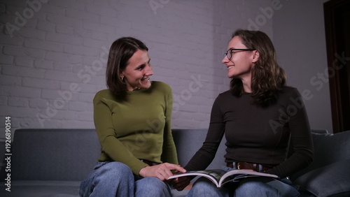 Bilde på lerret Two young women, appearing as sisters or close friends, sitting on a sofa and ha