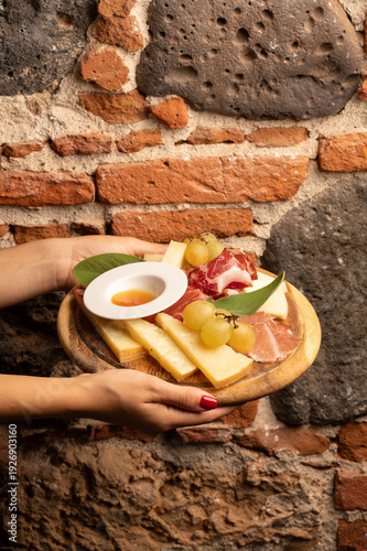 Fotografía Hands holding charcuterie board with cheese and prosciutto