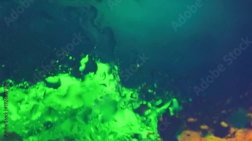 Vibrant green liquid splashing against a dark blue background with hints of orange, captured in a close-up abstract composition with a shallow depth of field.