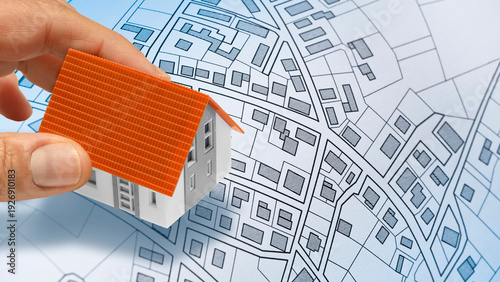 HAND PLACING A MODEL HOUSE ON AN URBAN MAP CONCEPT - Architectural planning and real estate development concept with property layout, residential zoning, and construction project design