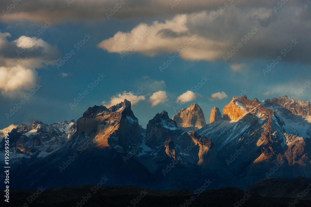 Obraz premium Majestic granite peaks of the Cuernos del Paine at sunset with golden light hitting the mountain tops under a dramatic sky in Patagonia, Chile.