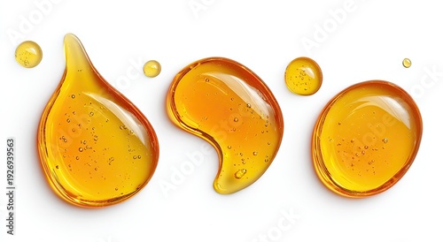 Several glossy, amber liquid drops and puddles of varied shapes against a white backdrop