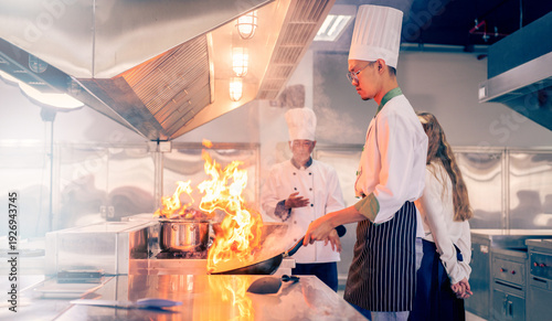 Tablou pe pânză Senior male chef teaches young teenage boys cooking in school kitchen