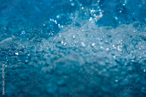 Macro shot of fresh blue water splashing with bubbles and water droplets. Abstract turquoise liquid background representing purity, freshness, and hydration. High-speed photography of water surface ri