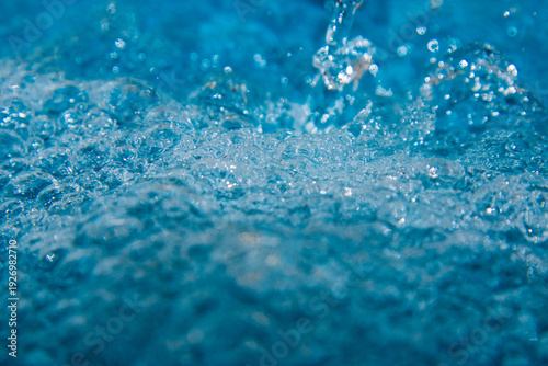 Macro shot of fresh blue water splashing with bubbles and water droplets. Abstract turquoise liquid background representing purity, freshness, and hydration. High-speed photography of water surface ri