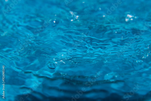Macro shot of fresh blue water splashing with bubbles and water droplets. Abstract turquoise liquid background representing purity, freshness, and hydration. High-speed photography of water surface ri