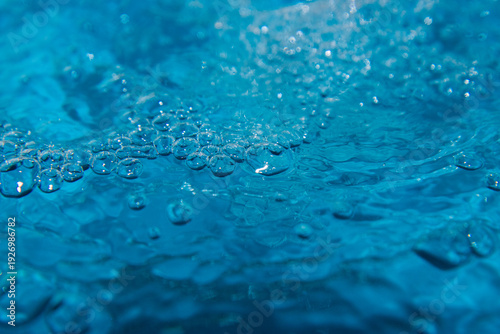 Macro shot of fresh blue water splashing with bubbles and water droplets. Abstract turquoise liquid background representing purity, freshness, and hydration. High-speed photography of water surface ri