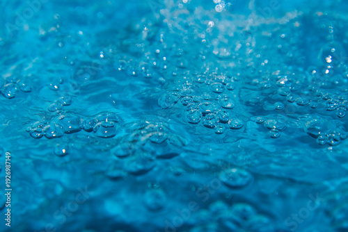 Macro shot of fresh blue water splashing with bubbles and water droplets. Abstract turquoise liquid background representing purity, freshness, and hydration. High-speed photography of water surface ri