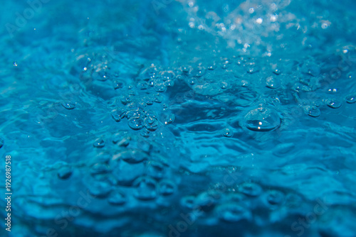 Macro shot of fresh blue water splashing with bubbles and water droplets. Abstract turquoise liquid background representing purity, freshness, and hydration. High-speed photography of water surface ri