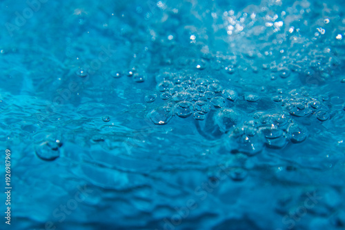 Macro shot of fresh blue water splashing with bubbles and water droplets. Abstract turquoise liquid background representing purity, freshness, and hydration. High-speed photography of water surface ri