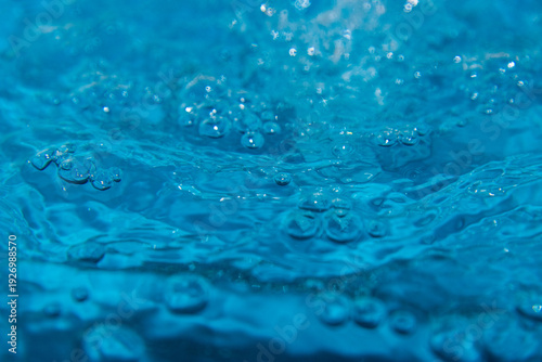 Macro shot of fresh blue water splashing with bubbles and water droplets. Abstract turquoise liquid background representing purity, freshness, and hydration. High-speed photography of water surface ri