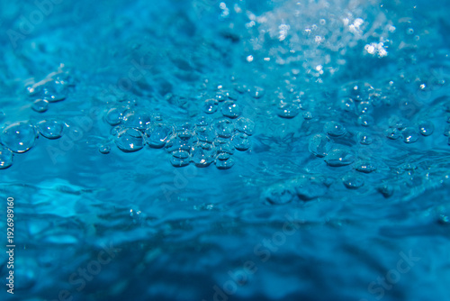 Macro shot of fresh blue water splashing with bubbles and water droplets. Abstract turquoise liquid background representing purity, freshness, and hydration. High-speed photography of water surface ri