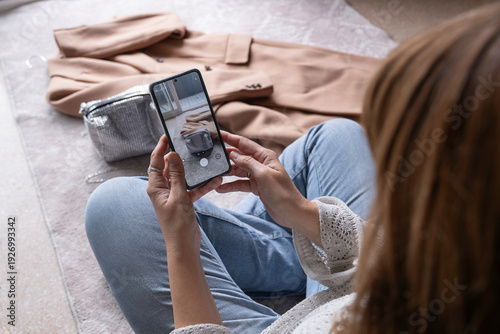 An anonymous woman taking photos of secondhand clothes with her mobile phone to sell online in a thrift store