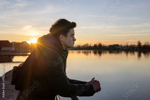 Foto Teenage boy sitting outdoors near water at sunset, looking thoughtful