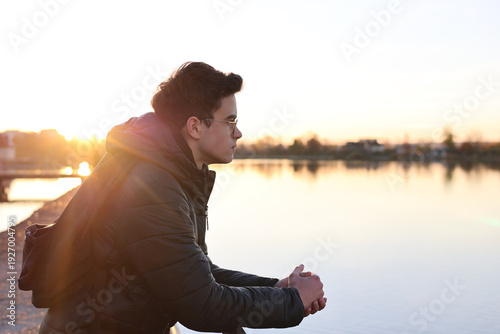 Photography Teenage boy sitting outdoors near water at sunset, looking thoughtful