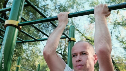 A middle-aged man performs pull-ups on a bar at a sports ground. Perfect 4K video for fitness, workout, and healthy lifestyle content.