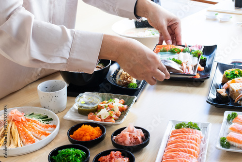 Lifestyle shot of hands placing a fresh sashimi platter onto a table filled with various Japanese dishes, a colorful and vibrant meal set.