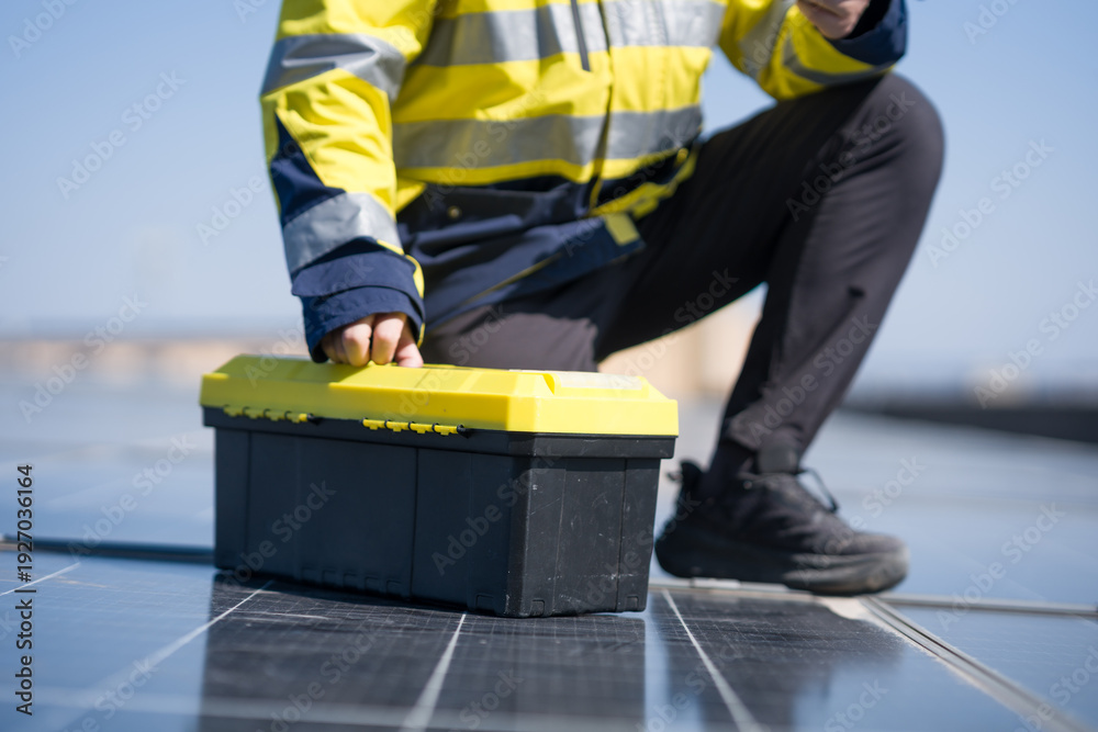 Fototapeta premium Worker crouching beside solar panels while opening a yellow toolbox