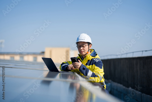 Engineer conducting on-site inspection of solar panels on rooftop using laptop and smartphone