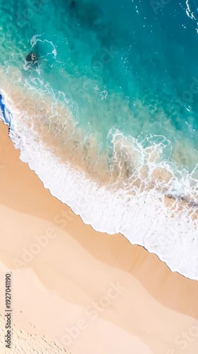 Aerial view of gentle turquoise ocean waves crashing on a golden sandy beach with rock formations.