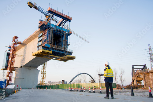Fotografie Construction worker directing girder installation during bridge building under c