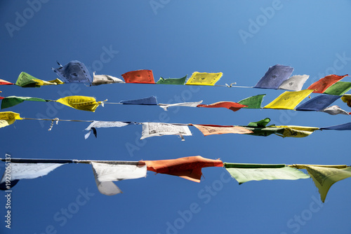 Colorful tibetan prayer flags hang in the blue sky above a buddhist temple during the day showcasing cultural significance and spirituality