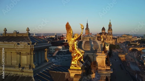 A circular aerial shoot of the statue of golden angel Phantasosone on the western corner risalit of the Dresden Art Academy  in the Lipsiusbau building under sunshine at dawn with the Frauenkirche, Dr