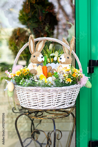 Easter basket with two plush bunny toys, flowers and decorative eggs on a metal stand