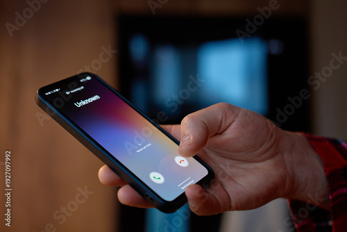 Closeup of hand holding smartphone with unknown incoming call on screen indoors. Concept of mobile communication, spam call and privacy risk