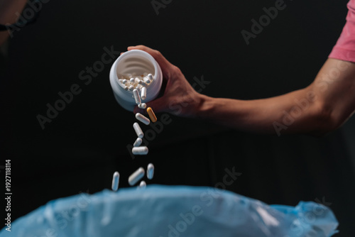 Slika na platnu Person hand discarding various pills and capsules from open white bottle into bl