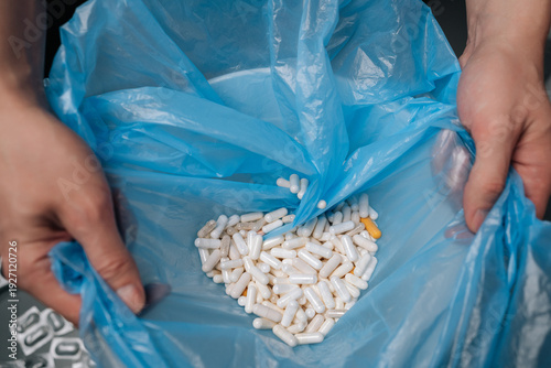 Slika na platnu Hands holding open blue plastic bag containing numerous discarded white and yell