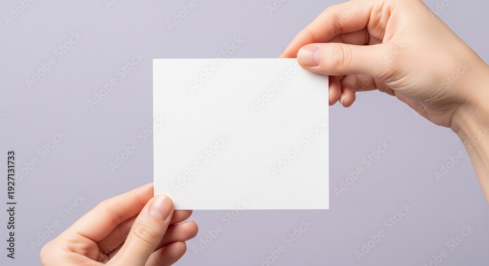 Obraz premium Hands holding a blank white card against a soft lavender background from a frontal viewpoint