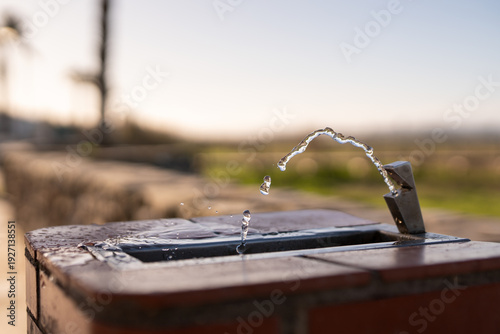 Fotografie Public drinking water fountain with flowing stream outdoors on sunny day represe