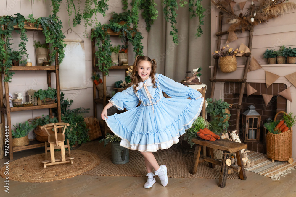 Obraz premium Happy little girl in blue dress. Smiling Kid girl dances and spins at home, cute child in festive outfit moves and rejoices against the background of the Easter interior room at home
