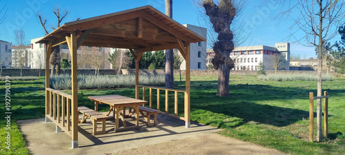 Obraz na płótnie Cenador de madera con mesa de picnic y bancos en un parque soleado con césped ve