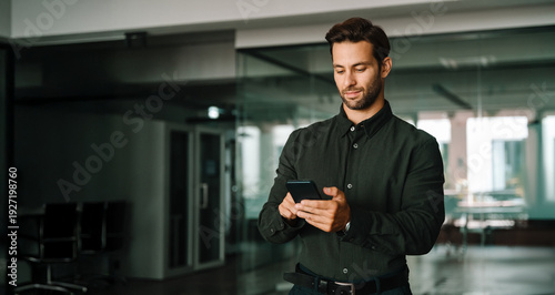 Fotografía Young businessman holding smartphone telephone device standing in office