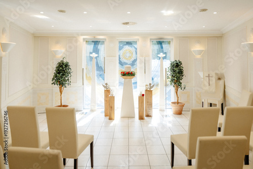 Solemn Funeral Hall with a Memorial Urn on a Pedestal, Surrounded by Candles and Floral Tributes in Soft Natural Daylight