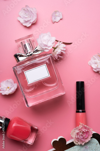 lady set with perfume and flowers around pink background. flat lay