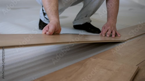 Worker aligning and clicking laminate floor panels together. Interior renovation and flooring installation process.