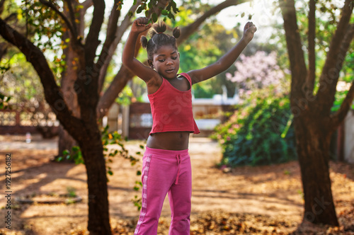 Young African Girl Jumping on Trampoline with Bantu Knots Hairstyle joyful expression while playing.