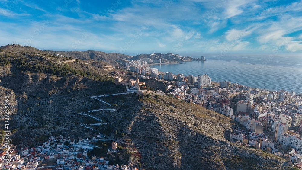 Obraz premium Wide aerial panorama of Cullera in Spain showing the Mediterranean coastline, river mouth and mountain ridge. Detailed drone view of seaside city, beaches and surrounding landscape.