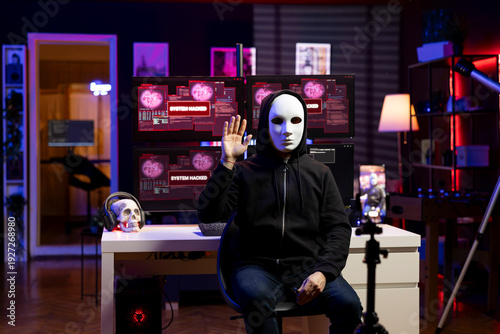 Fotografie Masked hacker greeting audience, filming ransom video in hidden home