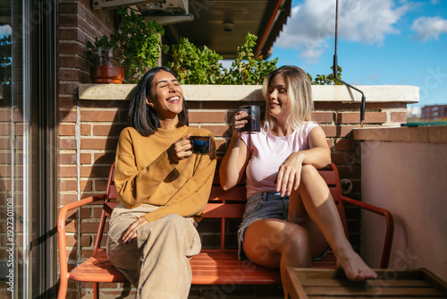Slika na platnu Lesbian couple laughing enjoying morning coffee on balcony