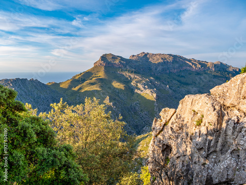 Rugged limestone peaks and terraced valleys showcase the raw beauty of Serra de Tramuntana mountain range on Mallorca island, captured in golden Mediterranean light perfect for travel content.