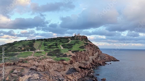 Aerial view of Temple of Poseidon on rocky cape Sounion cliff overlooking dramatic sea and cloudy sky, Greece
