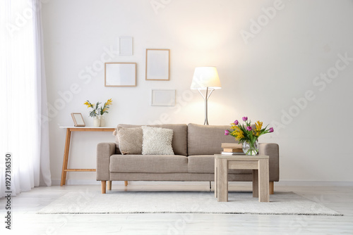 Interior of light living room with sofa, tables and spring flowers in vases
