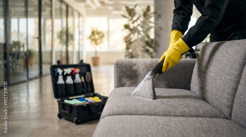 Professional cleaner in yellow gloves deep cleaning a sofa with an extractor machine in an office
