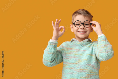 Little boy in eyeglasses showing OK on yellow background